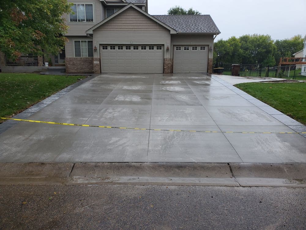 Freshly poured concrete driveway with yellow caution tape in front of a residential home.