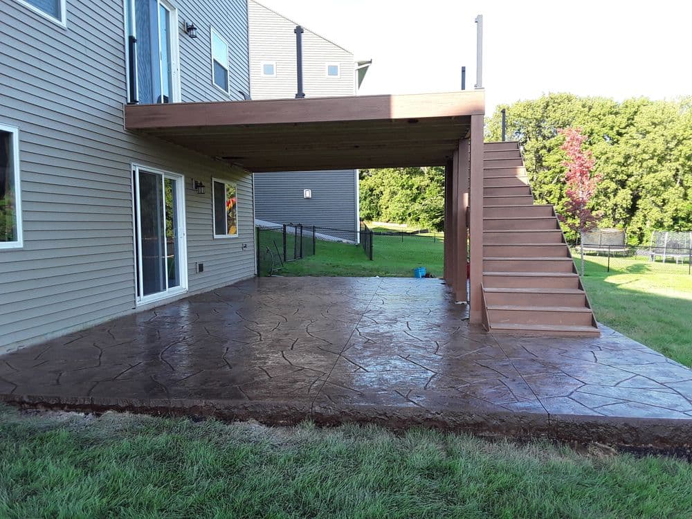Modern outdoor patio with stamped concrete and wooden deck stairs attached to a house.