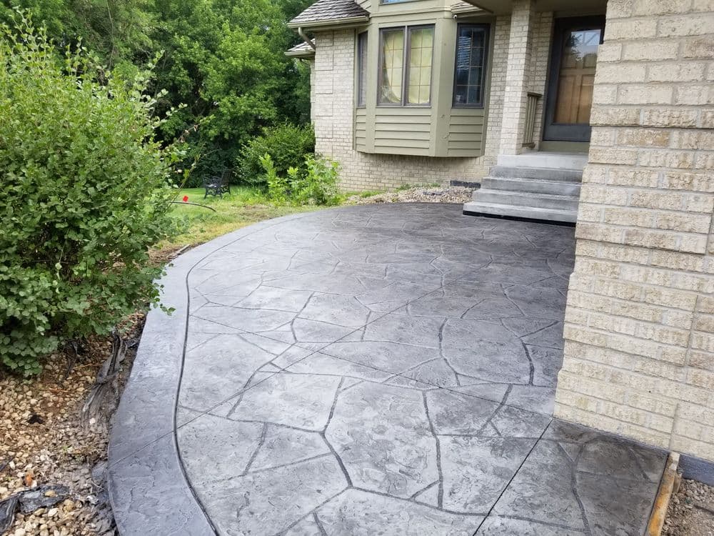Stylish stamped concrete walkway leading to a home entrance with greenery in the background.