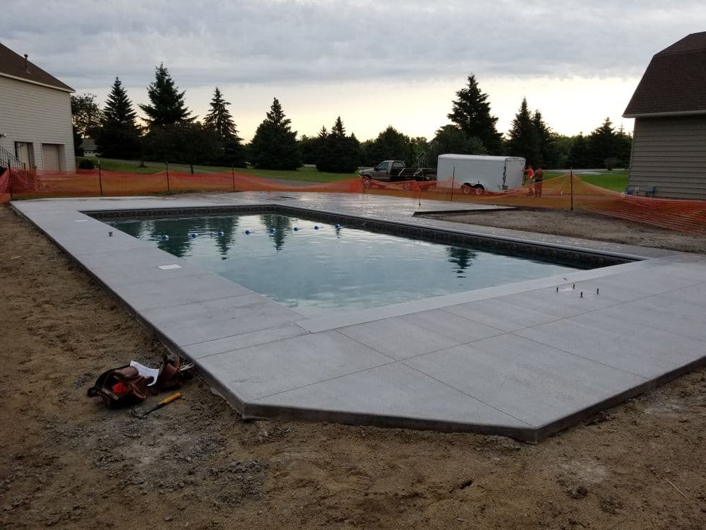 In-ground swimming pool installation with gray concrete surround and construction site details.