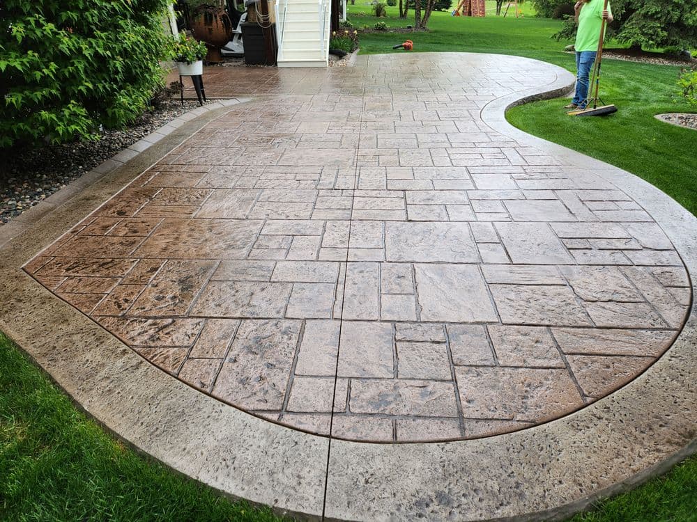 Decorative stamped concrete patio with intricate patterns and smooth finish in a landscaped yard.