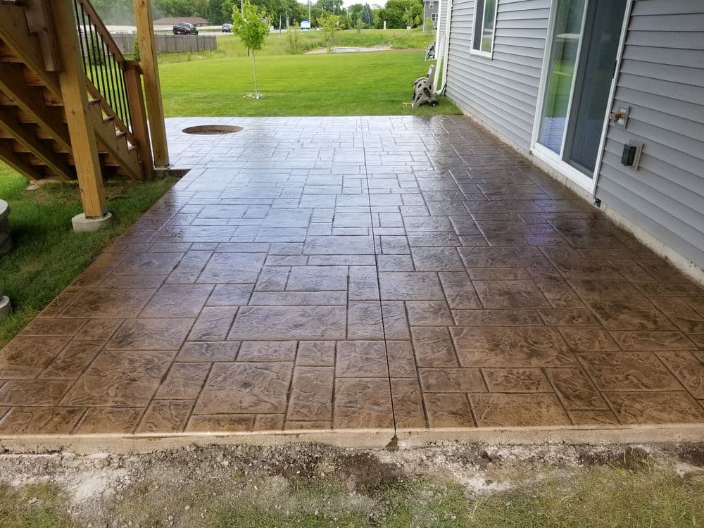 Stamped concrete patio with a smooth finish, surrounded by green grass and a house exterior.