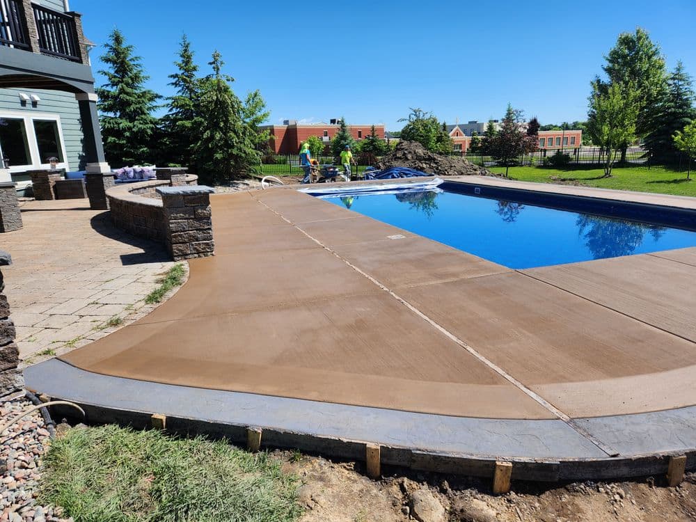 Poolside renovation with stamped concrete deck and workers preparing the area. Summer scene.