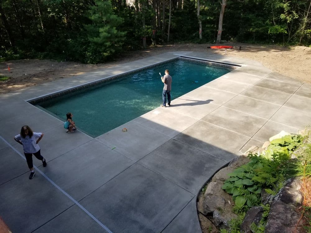 Family enjoying a freshly installed swimming pool in a forested backyard setting.