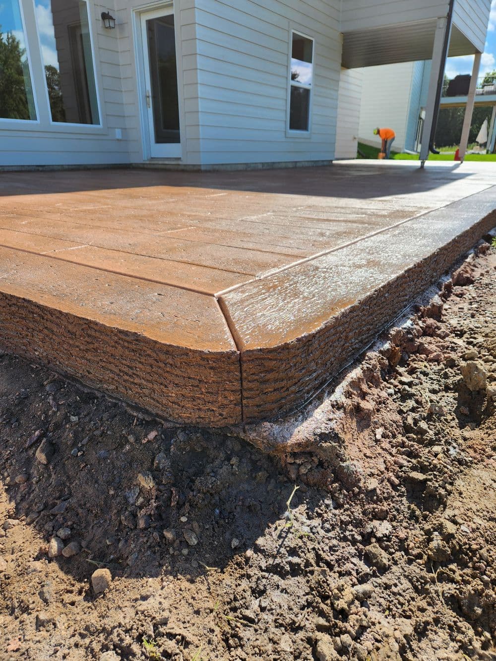 Newly poured decorative concrete patio with textured finish and landscaping in the background.