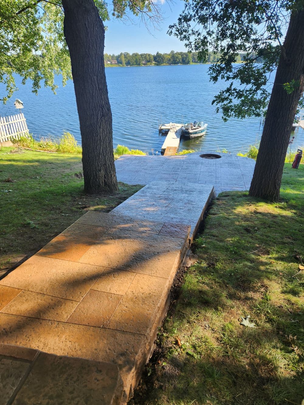 Pathway leading to a lake with a dock and boat, surrounded by trees and grass.
