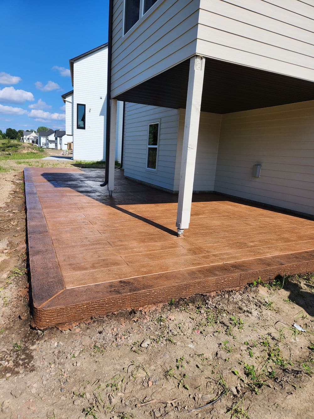 Newly constructed stamped concrete patio next to a modern house with clear blue sky.