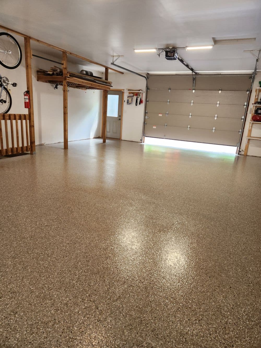 Spacious garage interior with epoxy floor, storage shelves, and natural light from bay door.