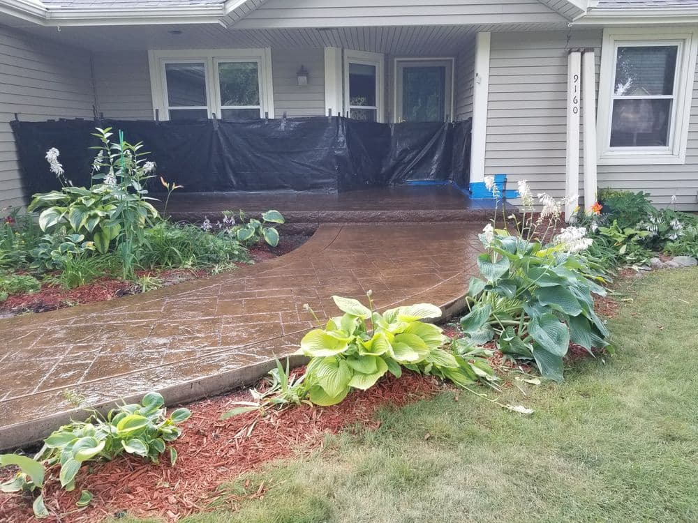 Front porch with stamped concrete walkway, landscaped garden, and black construction barrier.