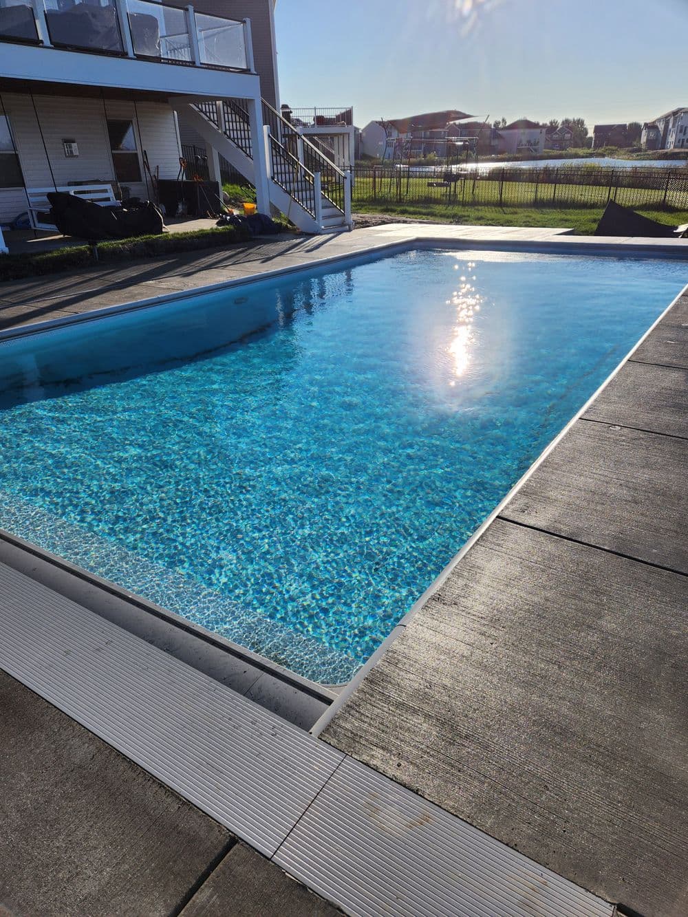 Clear blue swimming pool reflecting sunlight, surrounded by a well-maintained patio and grass.