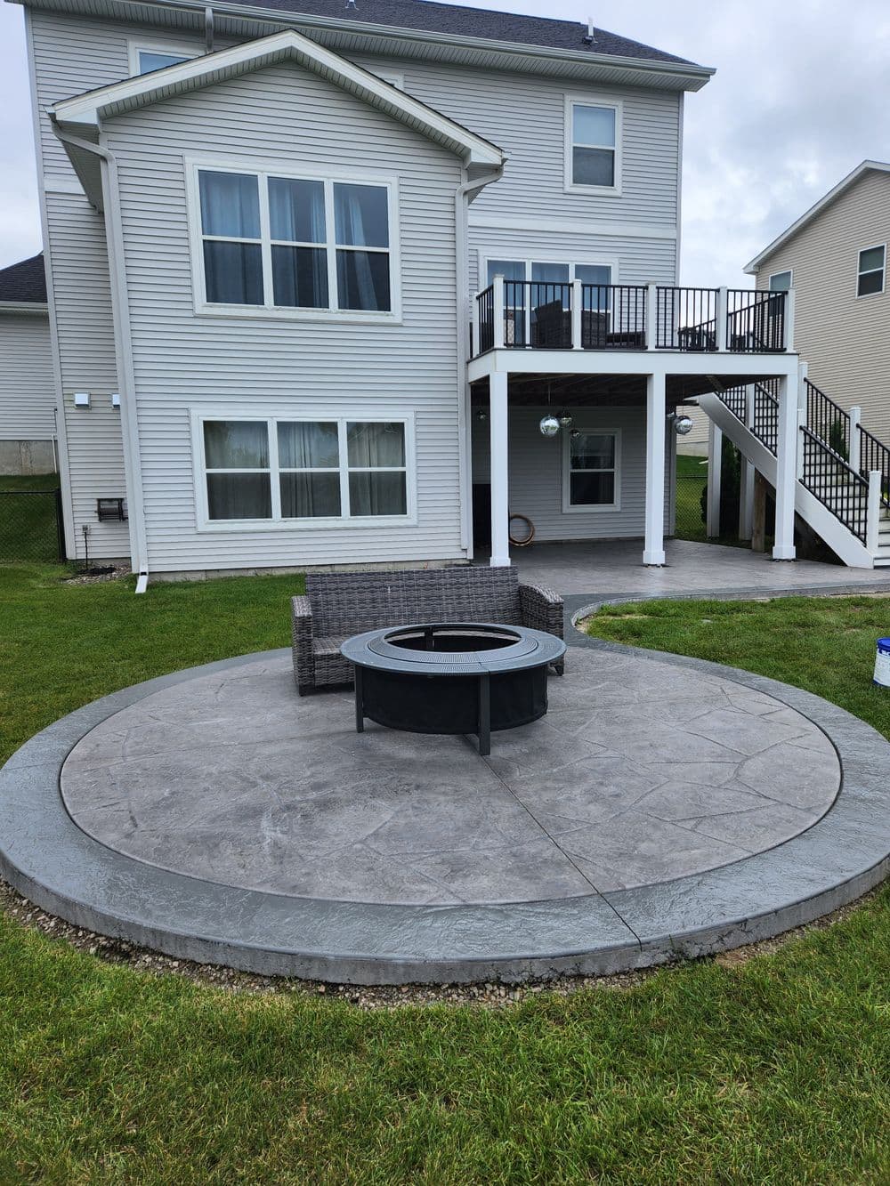 Backyard patio with circular fire pit and modern furniture under a home's deck.