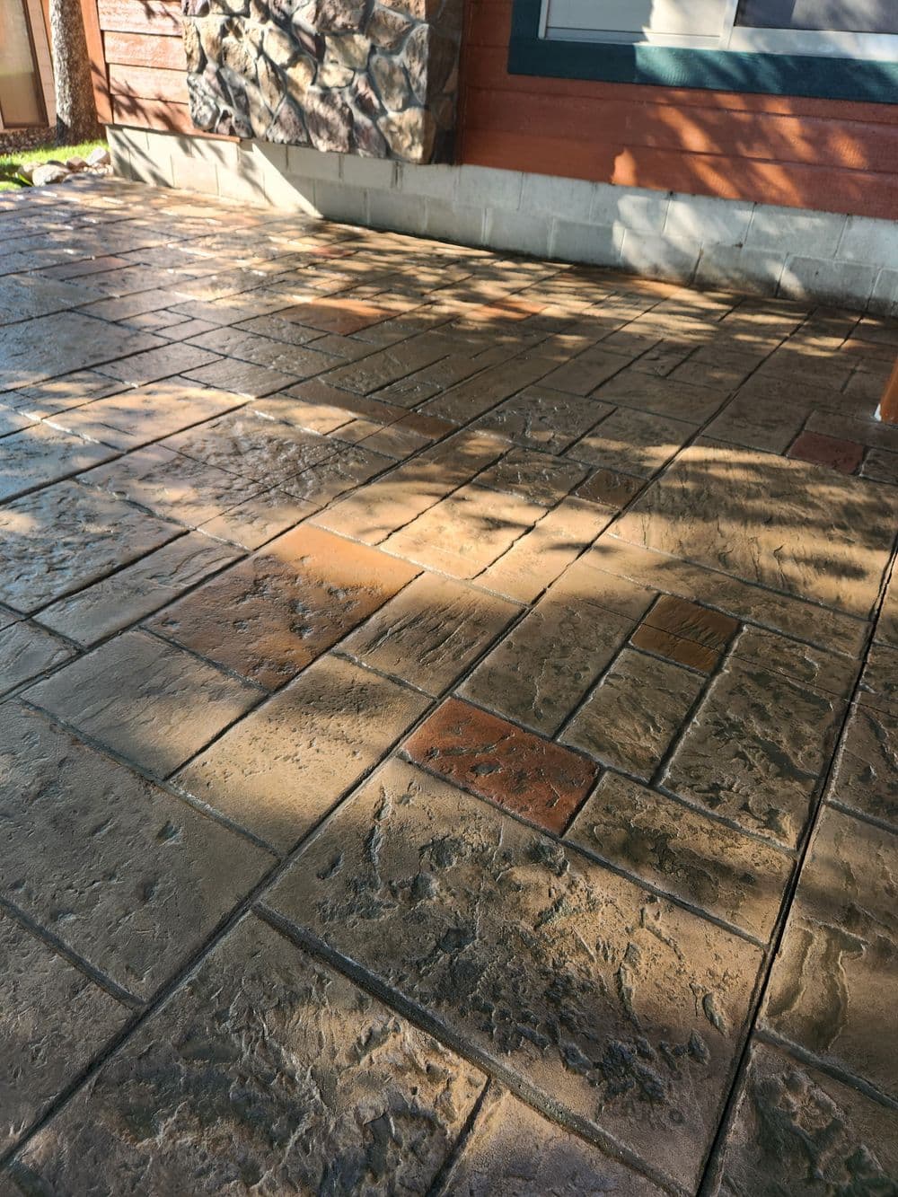 Textured stamped concrete patio with natural stone accents and sunlight shadows.