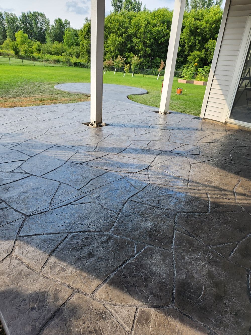 Textured stamped concrete patio with grassy landscape and trees in the background.