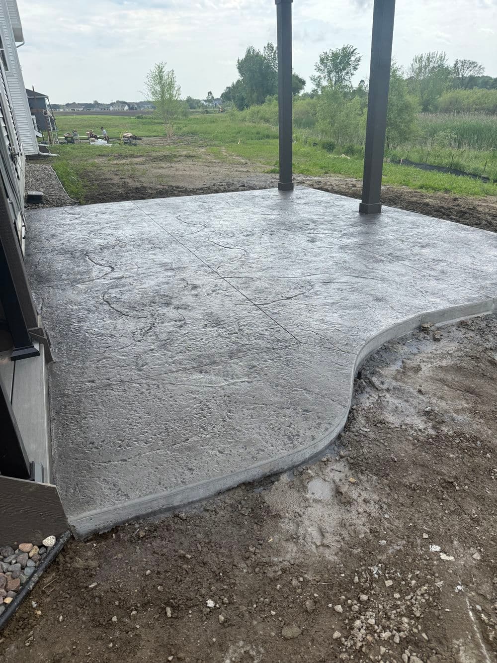 Concrete patio under construction with a curved edge, surrounded by green landscaping.