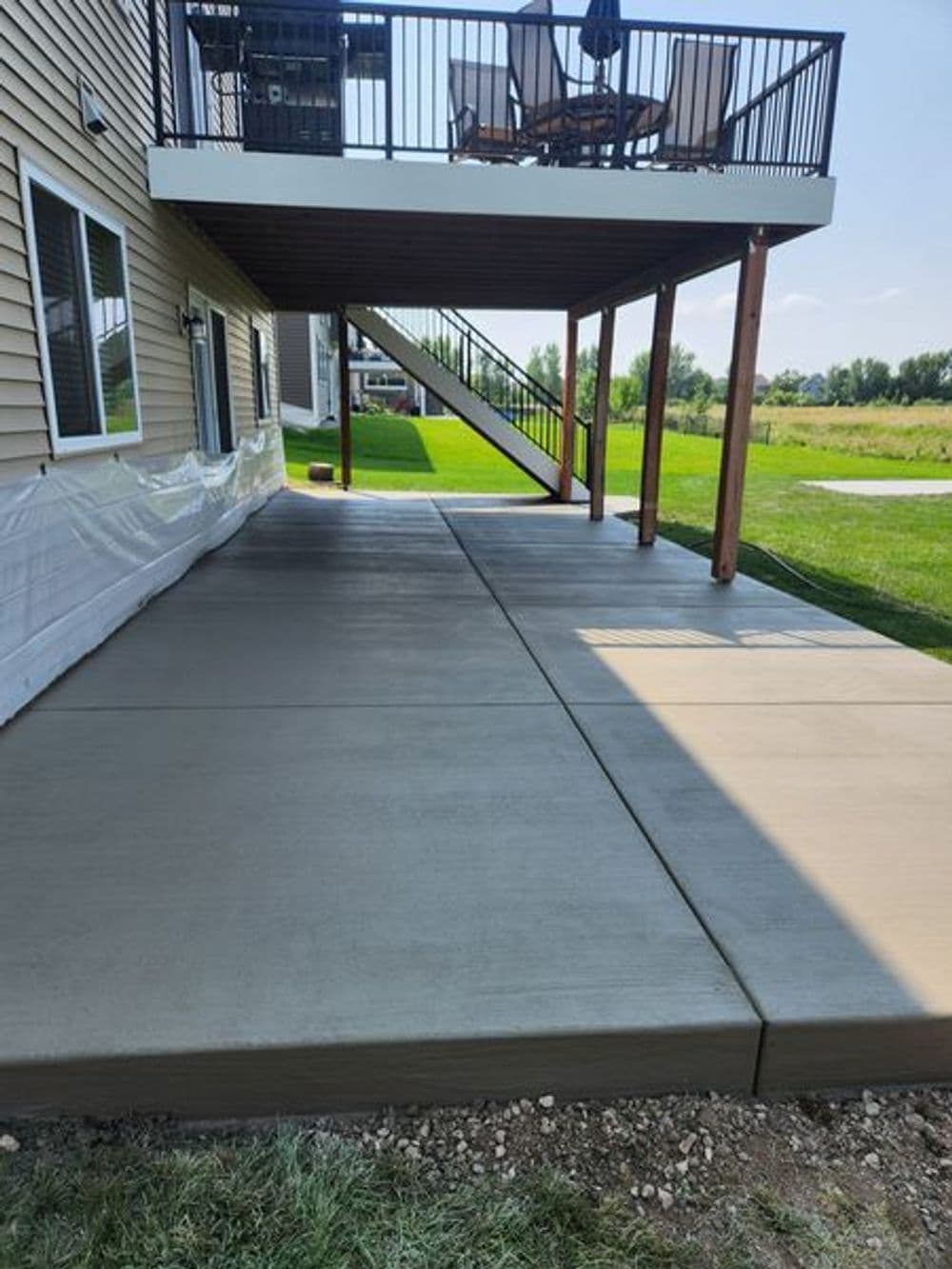 Newly poured concrete patio under a deck with grass and blue sky in the background.