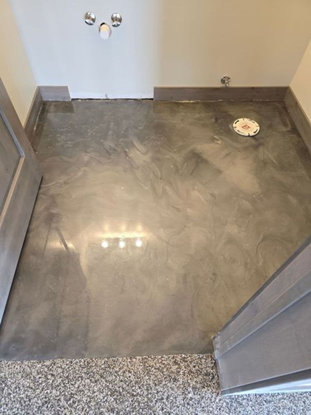 Concrete floor in a bathroom with drain, unfinished walls, and gray color scheme.