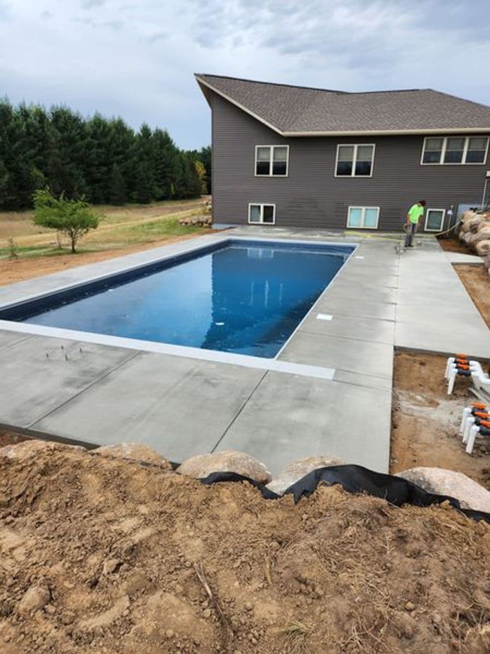 Modern in-ground swimming pool with concrete decking beside a newly constructed home.