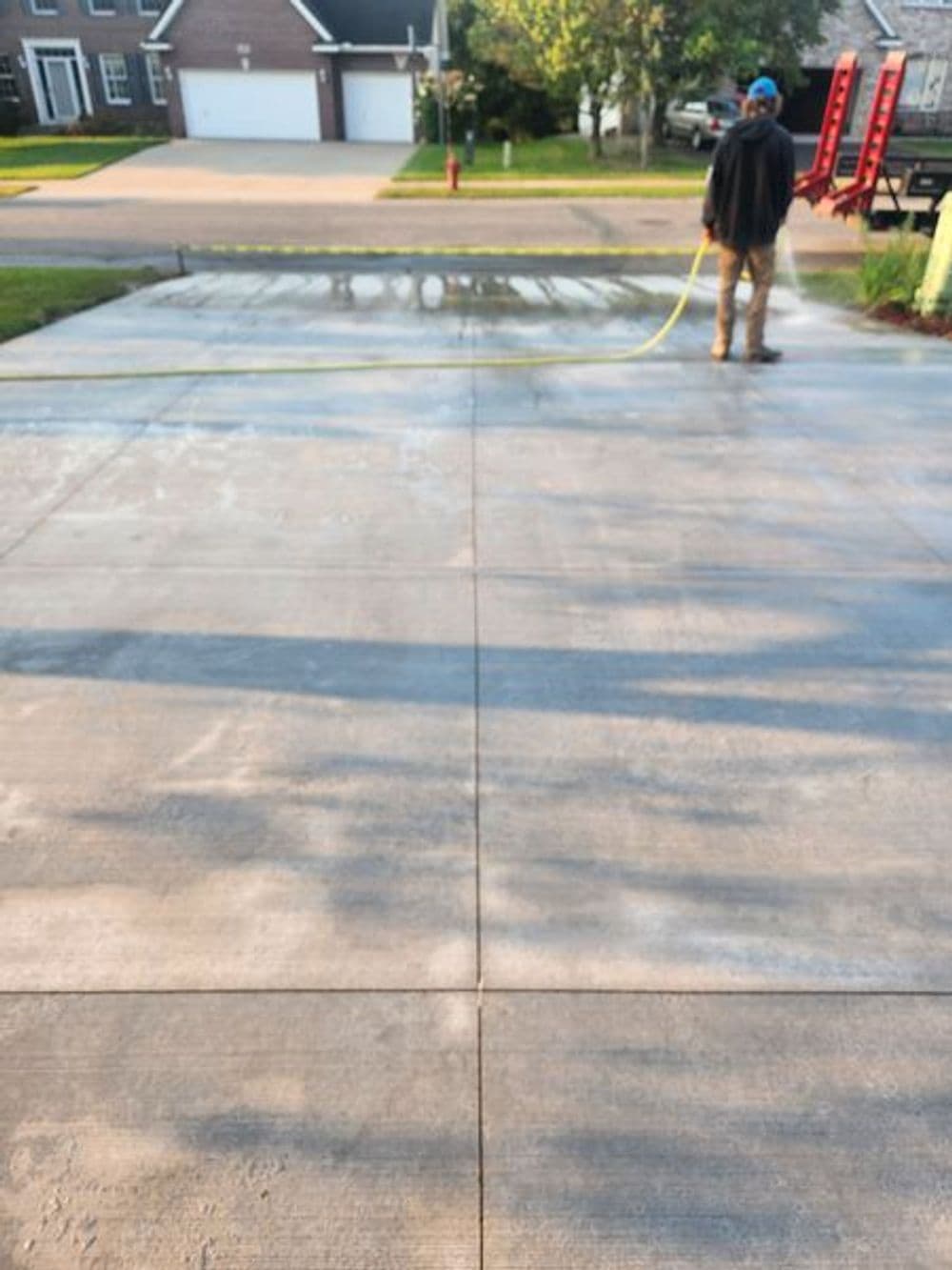 Person cleaning a concrete driveway with a hose, showing clear surface and residential setting.