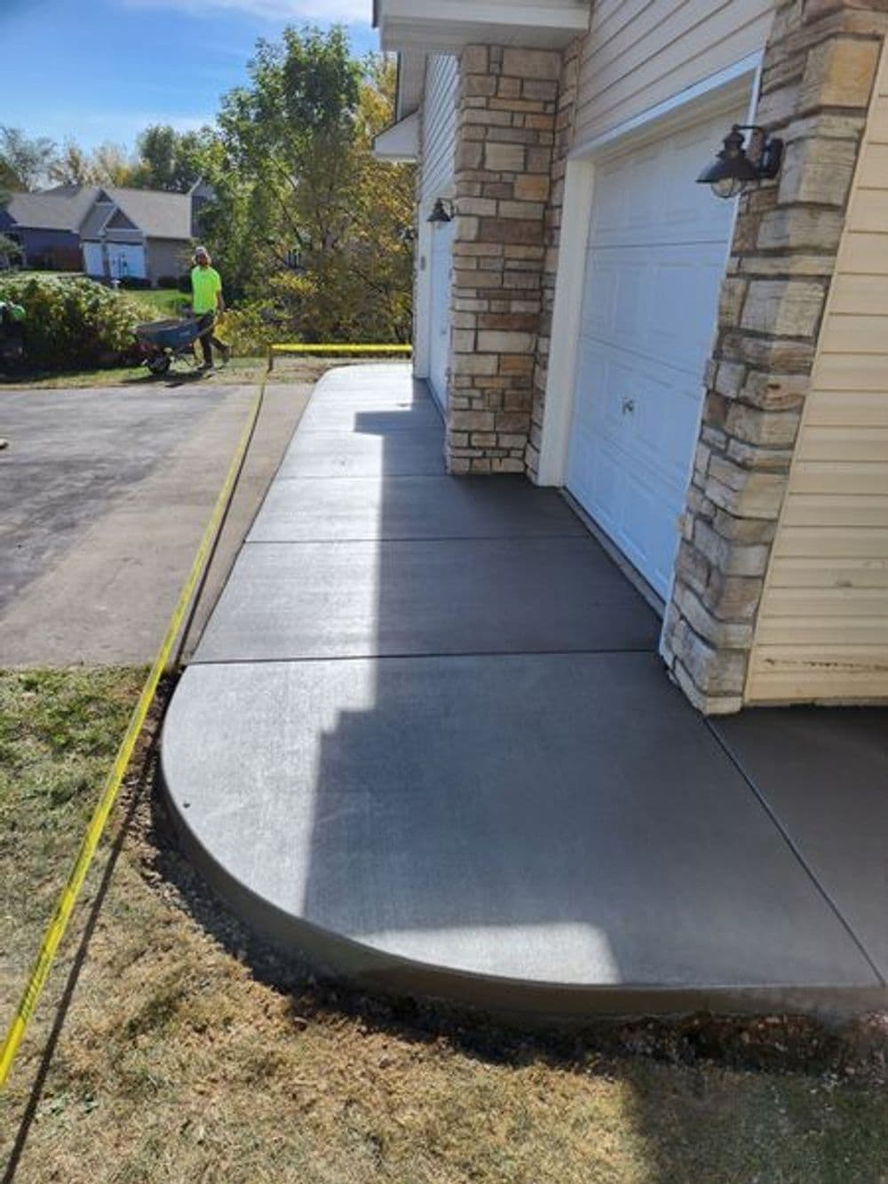 Concrete walkway installation alongside a house with a garage, featuring a rounded edge.