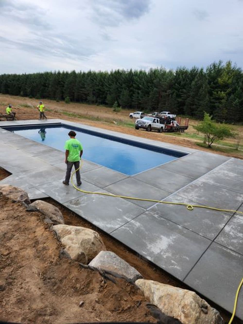 Construction workers installing a concrete swimming pool surrounded by trees and landscape.