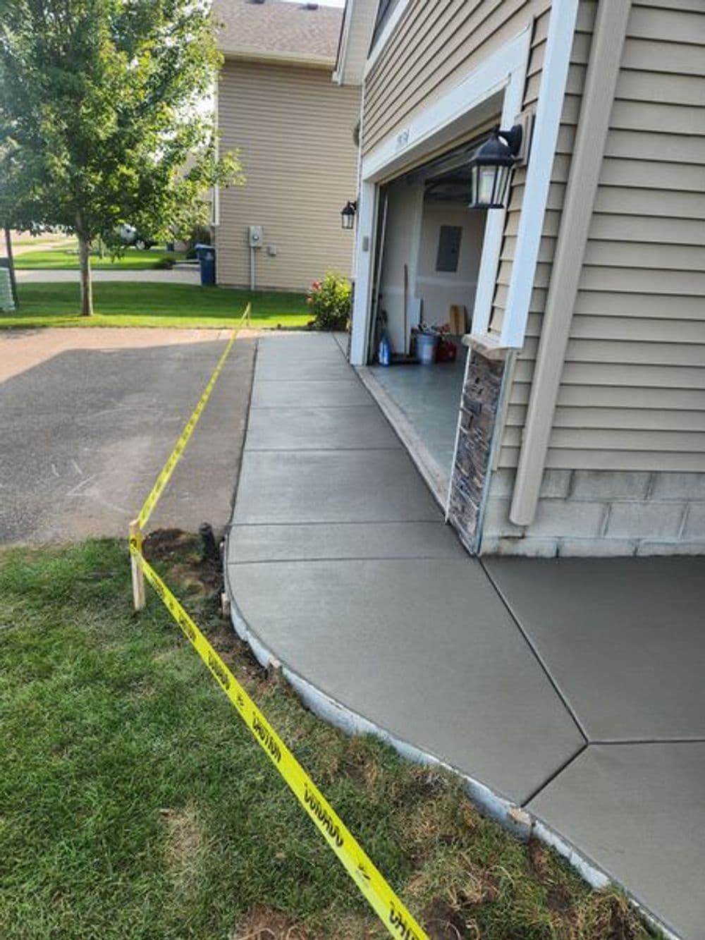 Freshly poured concrete sidewalk and garage entrance with caution tape in residential setting.