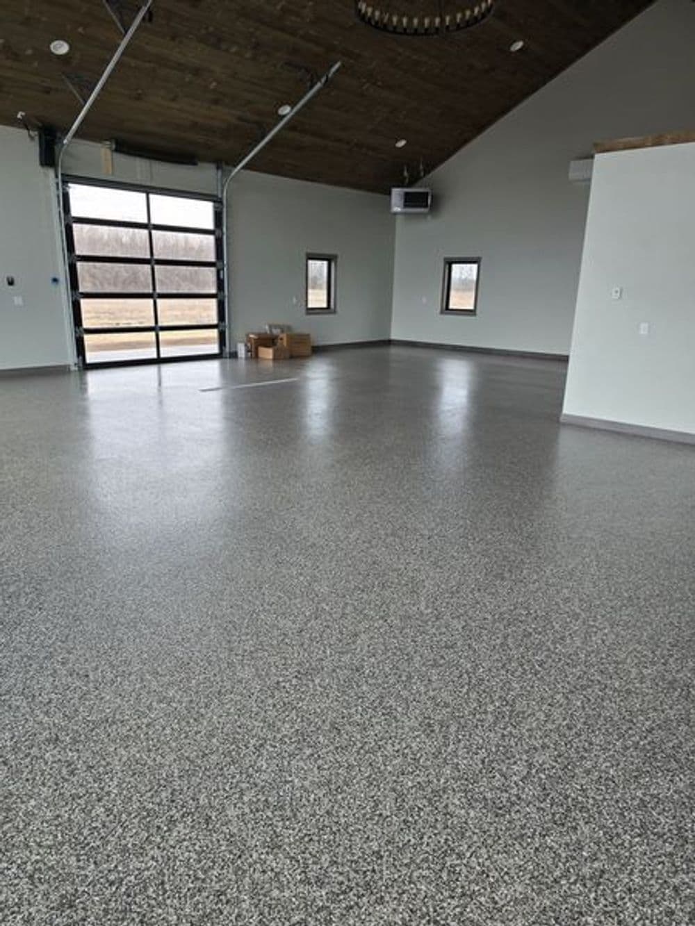 Spacious garage interior with gray epoxy flooring and large rolling door, featuring a modern design.