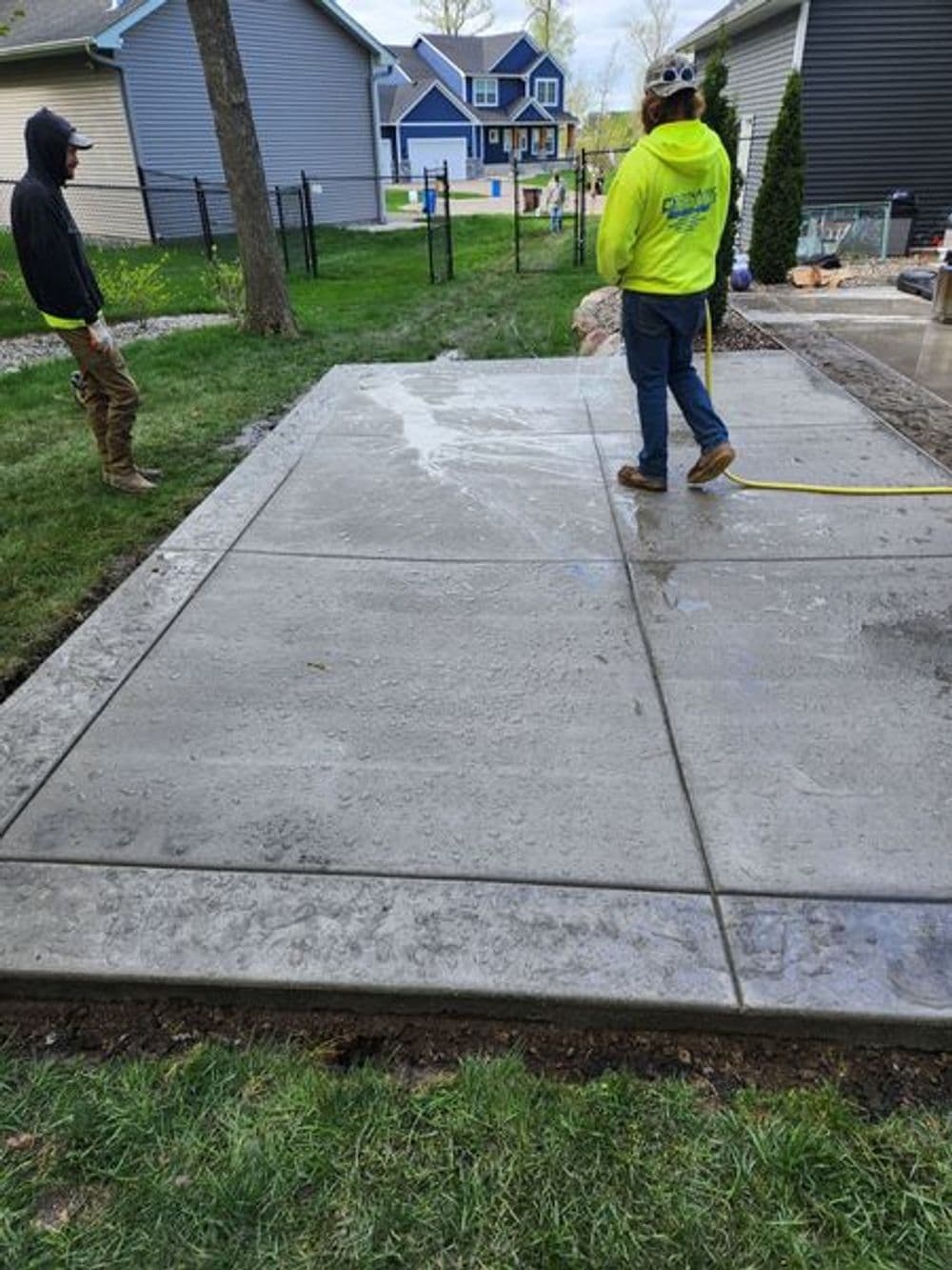 Construction workers applying finishing touches to a newly poured concrete slab in a backyard.