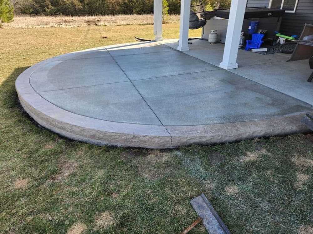 Newly installed concrete patio with decorative edging in a backyard setting.