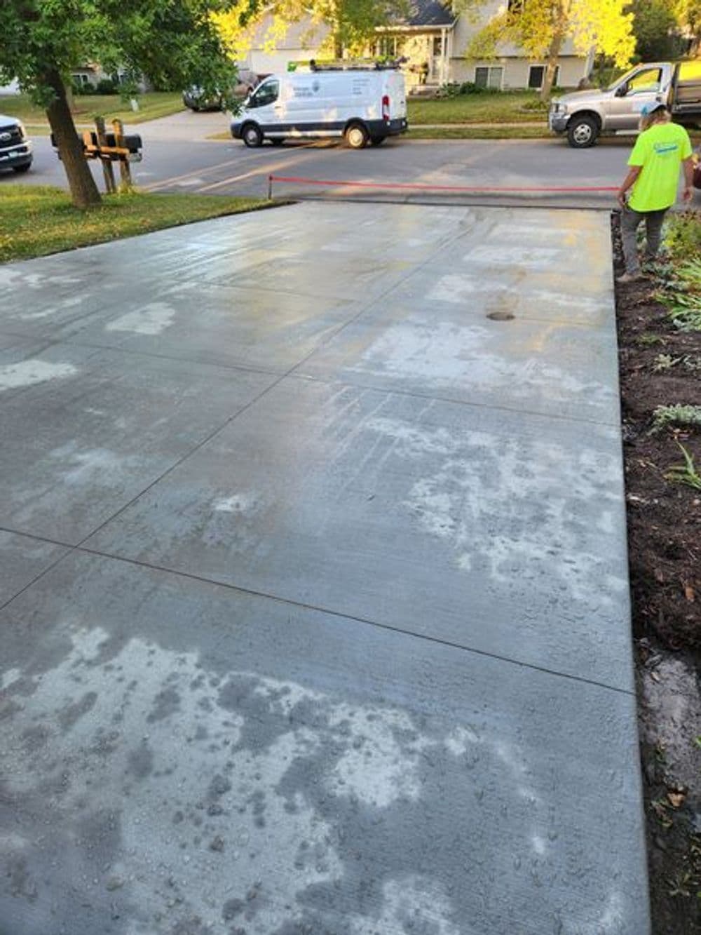 Freshly poured concrete driveway installation with workers and a van in the background.