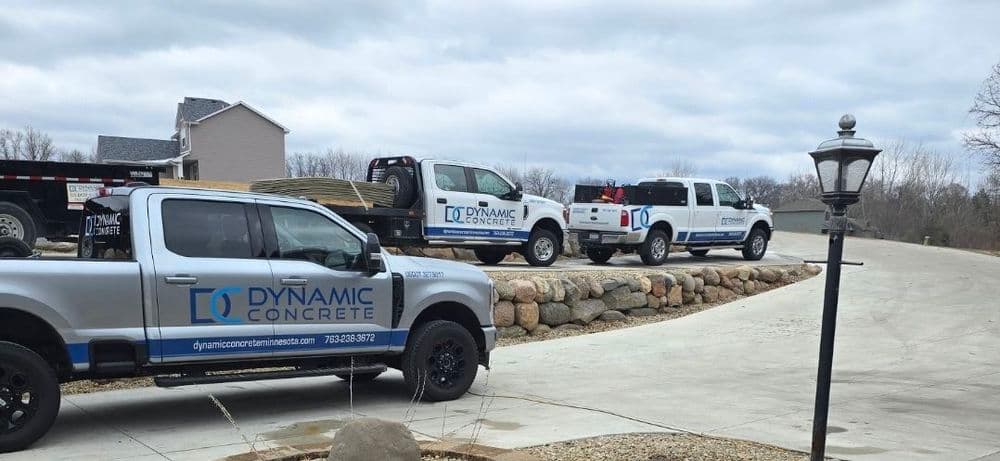 Dynamic Concrete trucks parked on a driveway, showcasing branded vehicles and landscaping materials.