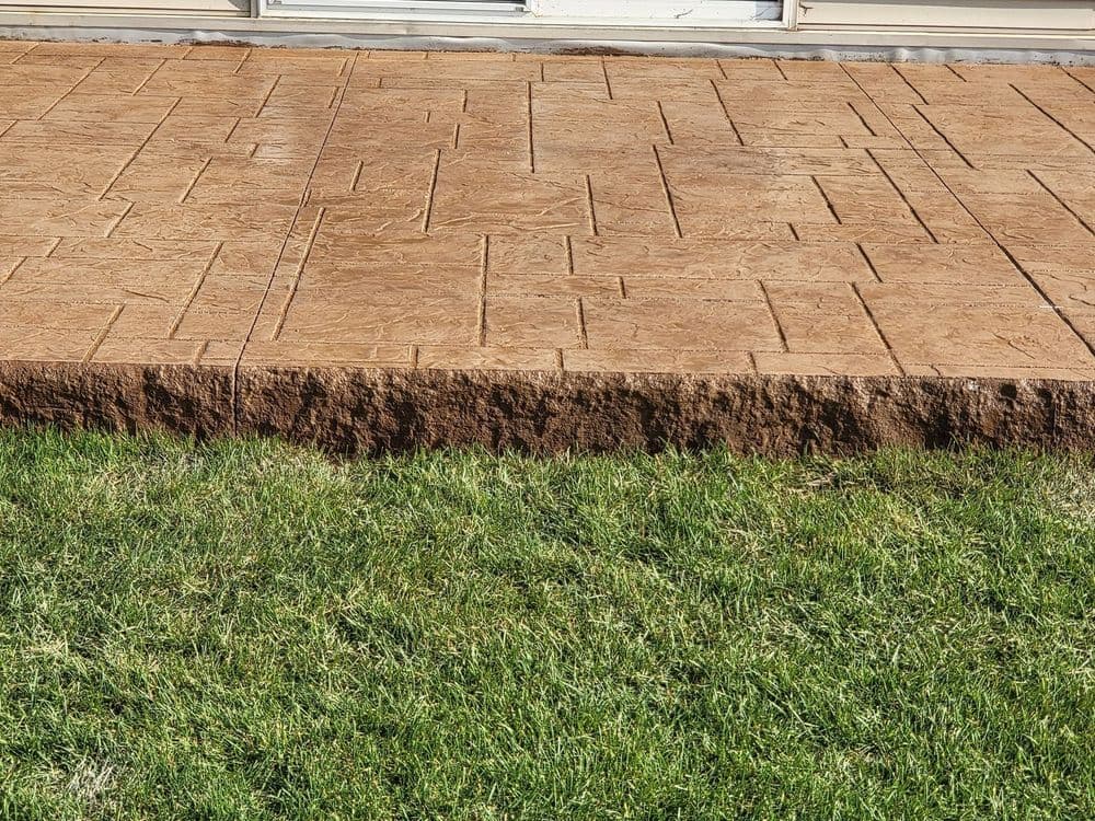 Textured brown stamped concrete patio next to green grass near a home.
