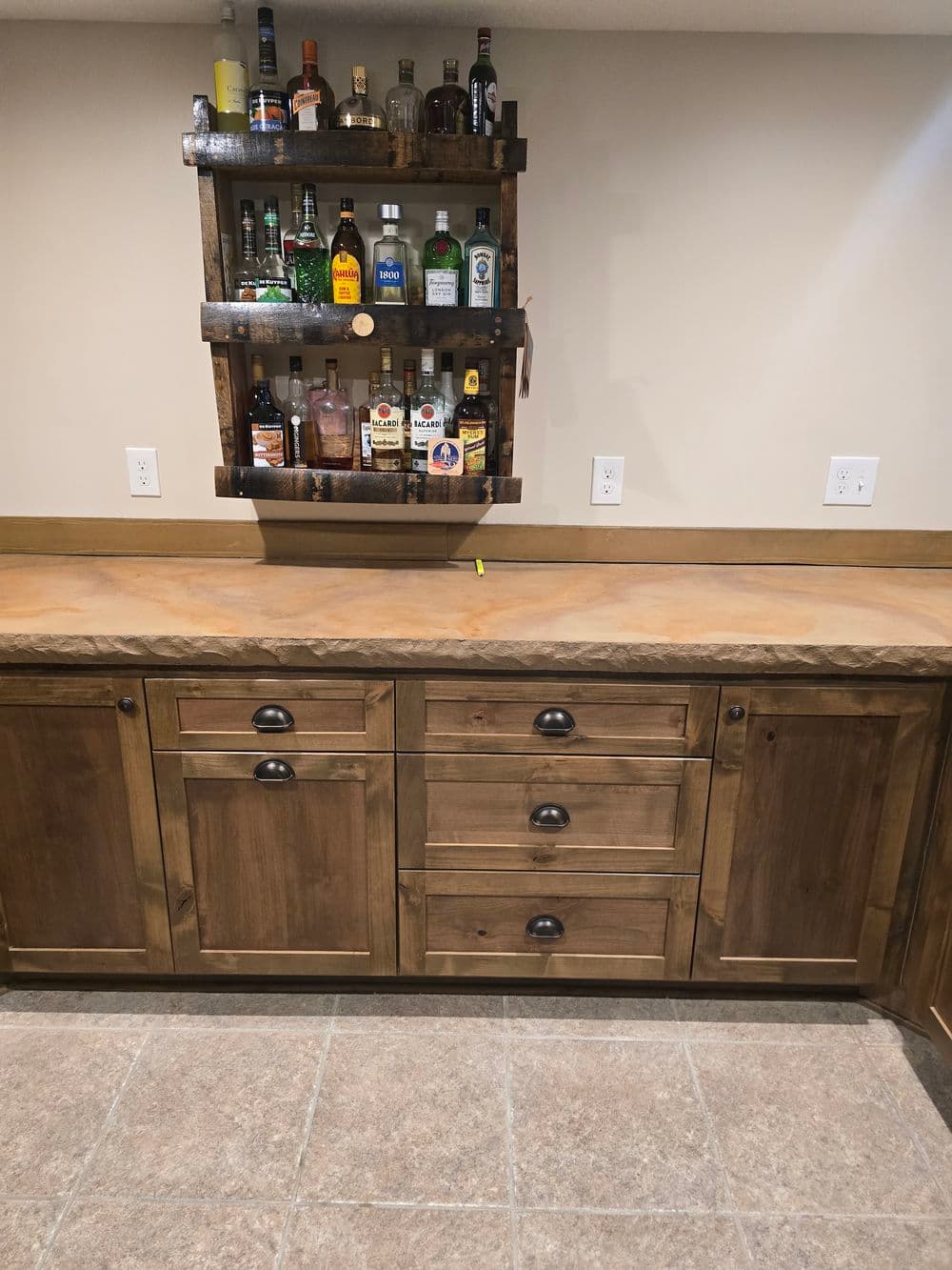 Wooden home bar with a variety of liquor bottles on a wall-mounted rack and a spacious countertop.