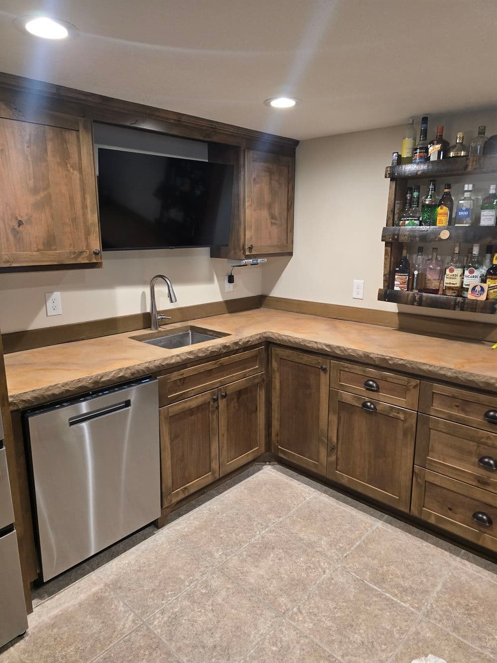 Modern basement kitchen with wooden cabinets, sink, stainless steel fridge, and wall-mounted bar.
