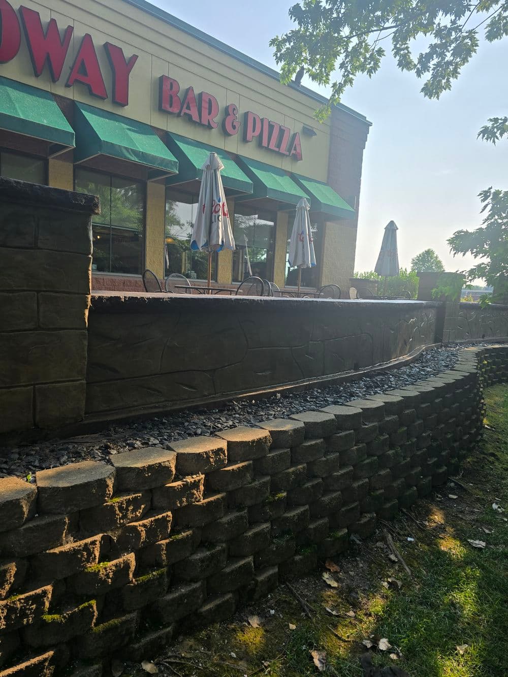 Exterior view of Broadway Bar & Pizza featuring outdoor seating and stone landscaping.