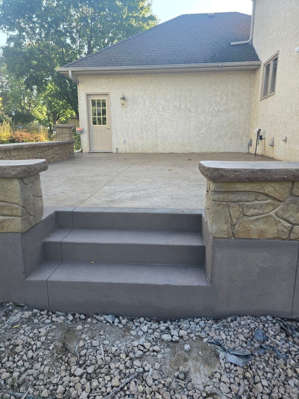 Concrete steps with stone accents leading to a back door and patio area.