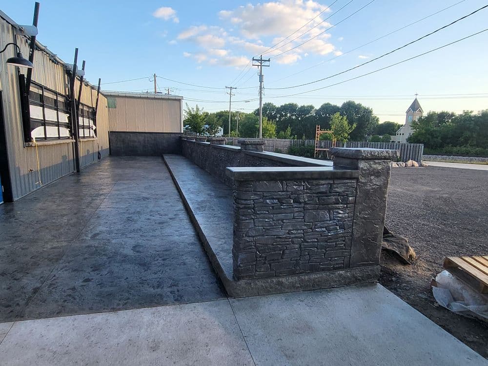 Outdoor concrete patio with stone walls and views of trees and power lines in the background.